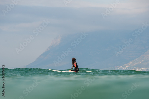 Surfer girl sits in the water with a mountain in the background
