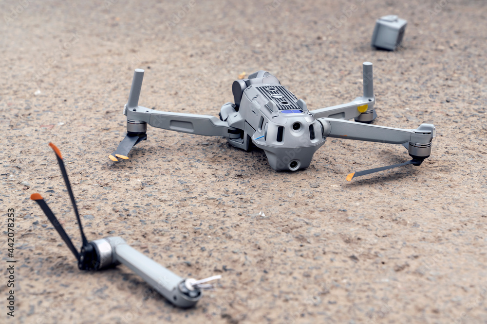 the fall of the drone. a broken flying quadcopter is lying on the asphalt,  the propeller has flown off and the camera is damaged Photos | Adobe Stock