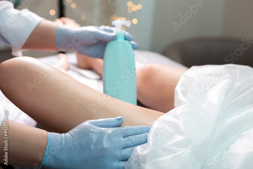 Professional Beautician Applying Soothing Cream on Female's Legs After Wax Depilation Procedure In Spa.