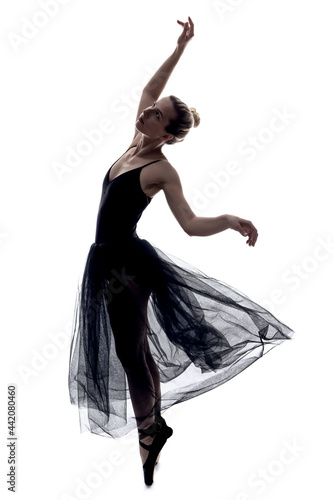 Dancing Caucasian Female in Body Suit and Light Black Dress Posing in Dance With Hands Lifted Against White.