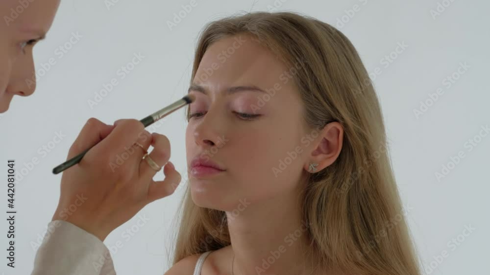 Stylist makeup artist doing makeup and hair in a beauty salon to Pretty model blonde. The work of a professional makeup artist. Concept of fashion or beauty. Close up. Stylist makeup artist doing makeup and hair in a beauty salon to Pretty model blonde. The work of a professional makeup artist. Concept of fashion or beauty. Close up.