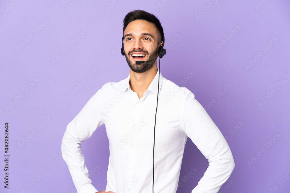 Telemarketer man working with a headset isolated on purple background posing with arms at hip and smiling Telemarketer man working with a headset isolated on purple background posing with arms at hip and smiling