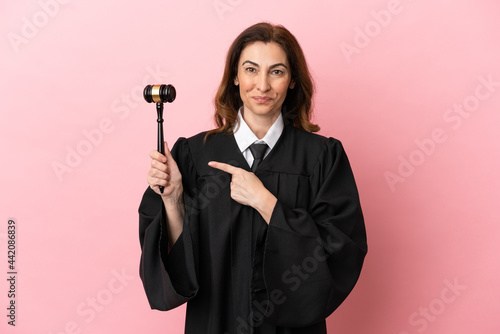 Fotografie, Tablou Middle aged judge woman isolated on pink background pointing to the side to pres