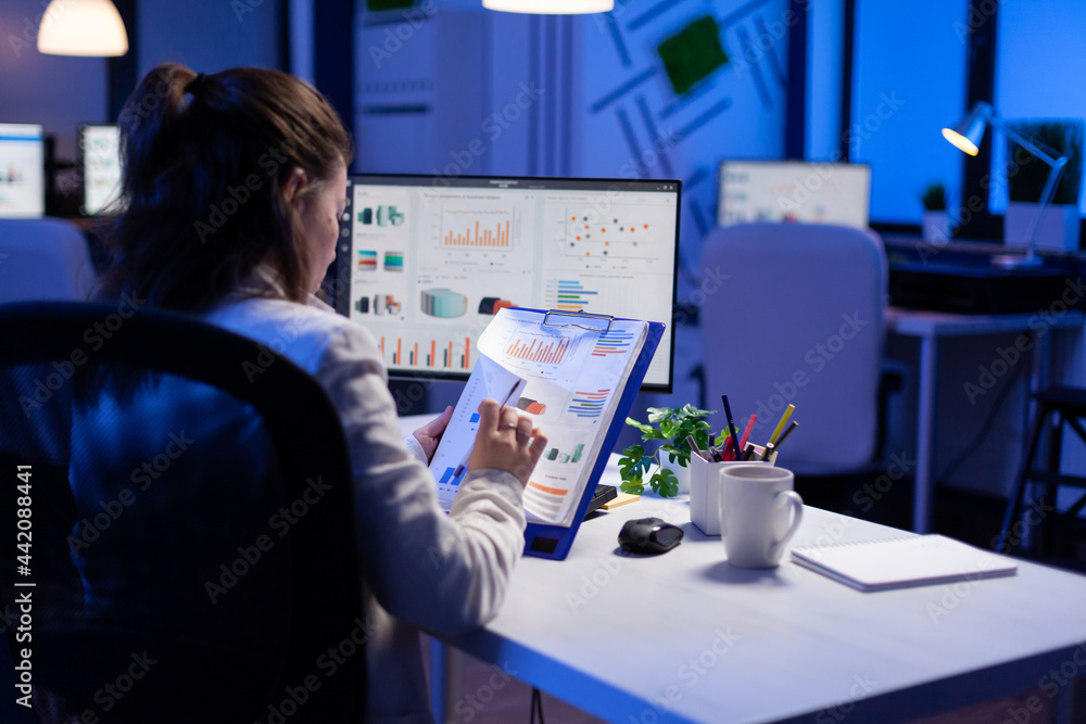 Freelancer woman comparing graphics from clipboard with grafics from computer at business office. Tired focused employee using modern technology network wireless working on project solution Freelancer woman comparing graphics from clipboard with grafics from computer at business office. Tired focused employee using modern technology network wireless working on project solution