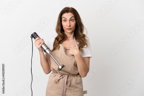 Middle aged caucasian woman using hand blender isolated on white background with surprise facial expression