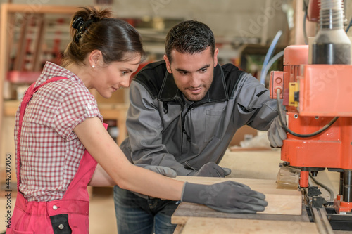 Male worker teaching female apprentice how to operate a machine