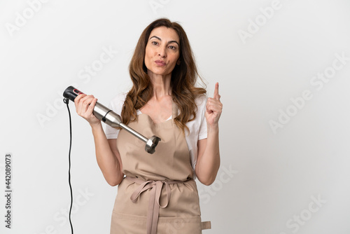 Middle aged caucasian woman using hand blender isolated on white background showing and lifting a finger in sign of the best