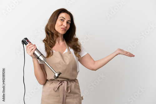 Middle aged caucasian woman using hand blender isolated on white background extending hands to the side for inviting to come