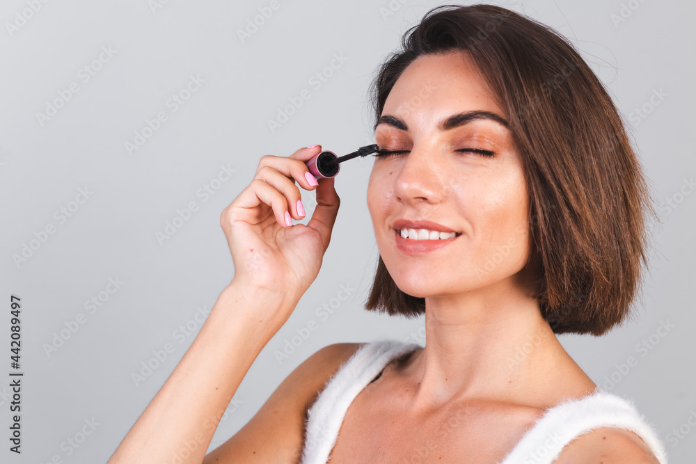 Beautiful woman with makeup hold black mascara brush on gray background, beauty concept