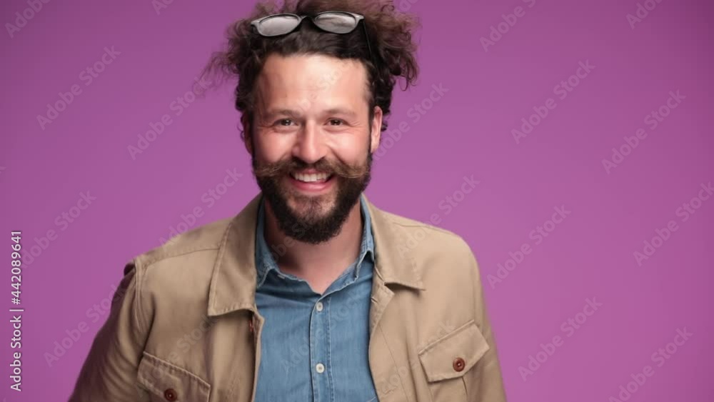 enthusiastic young man putting glasses on head, laughing, indicating to camera and making a hand gesture in studio on pink background enthusiastic young man putting glasses on head, laughing, indicating to camera and making a hand gesture in studio on pink background