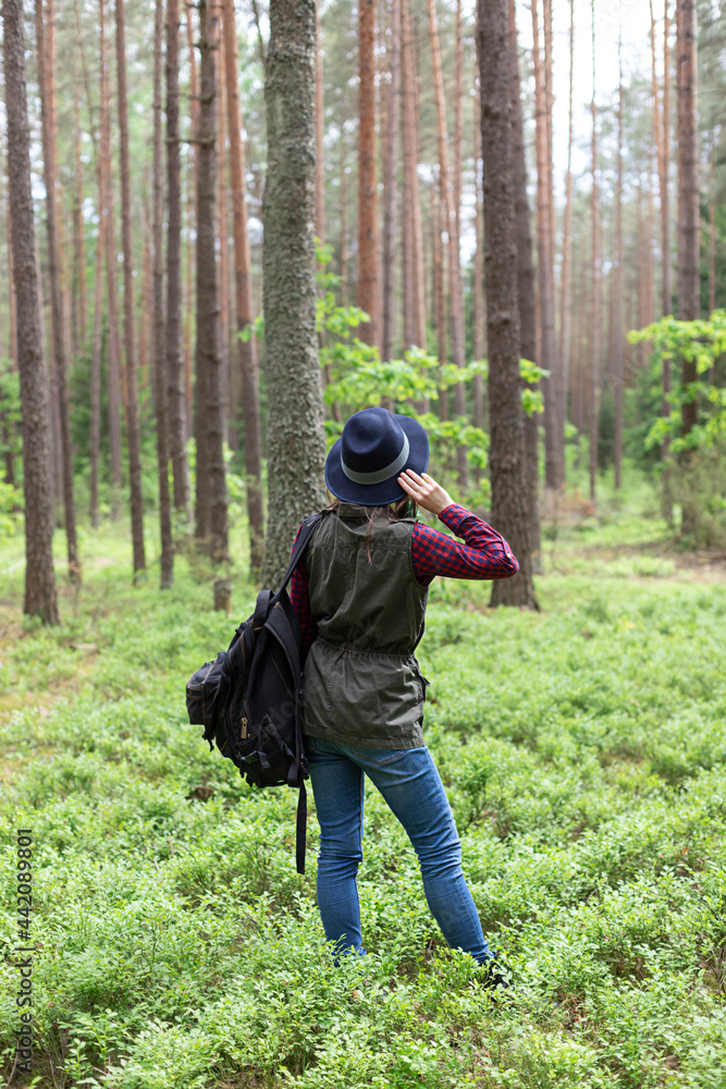 Young woman with black backpack holding the hat  while exploring  local nature. Hiking and travelling in forest concept