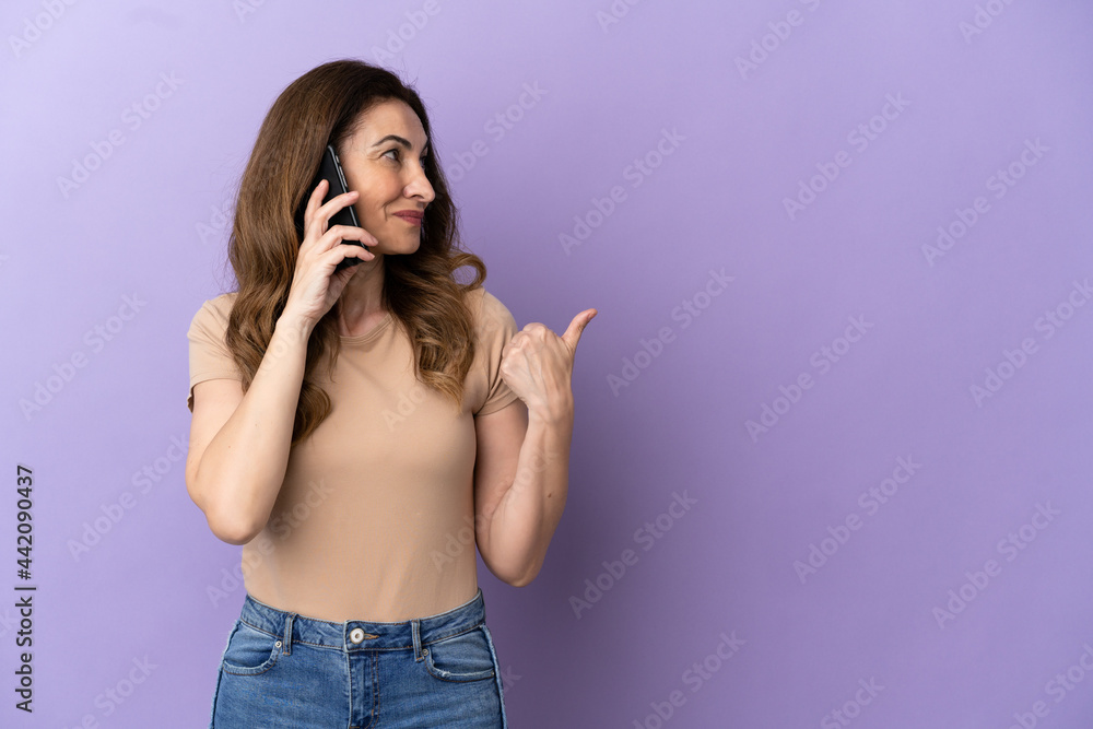 Middle aged caucasian woman using mobile phone isolated on purple background pointing to the side to present a product Middle aged caucasian woman using mobile phone isolated on purple background pointing to the side to present a product