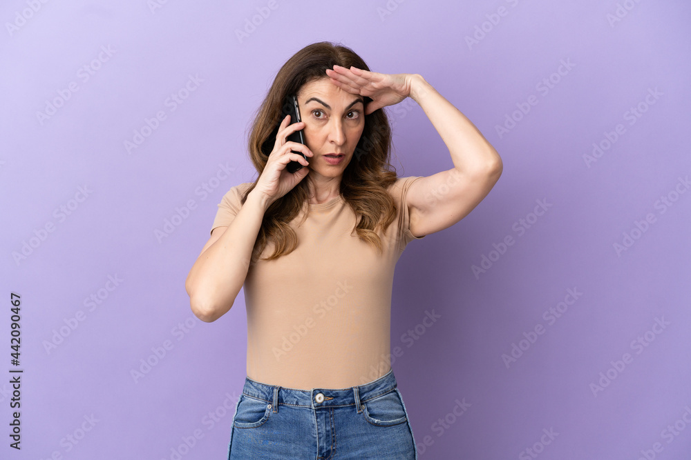 Middle aged caucasian woman using mobile phone isolated on purple background with surprise expression Middle aged caucasian woman using mobile phone isolated on purple background with surprise expression