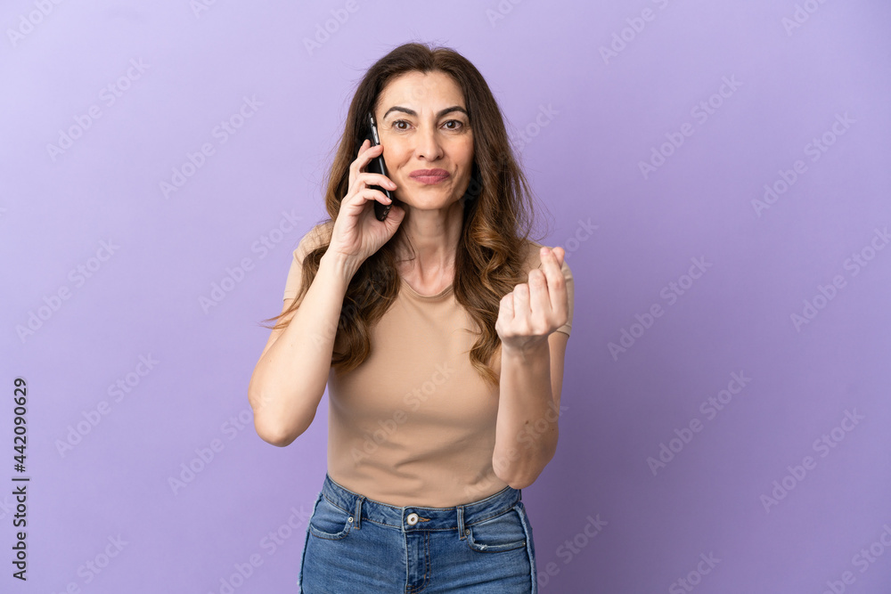 Middle aged caucasian woman using mobile phone isolated on purple background making money gesture Middle aged caucasian woman using mobile phone isolated on purple background making money gesture