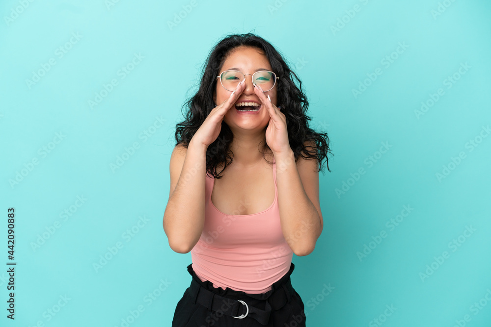 Young asian woman isolated on blue background shouting and announcing something Young asian woman isolated on blue background shouting and announcing something