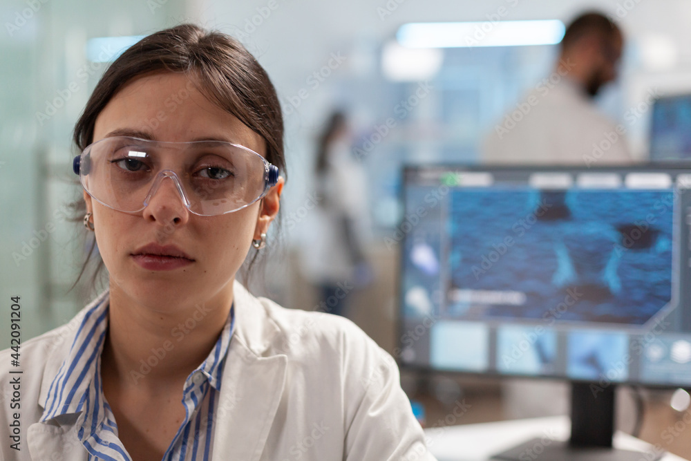 Exhausted microbiologist with protection glass sitting in laboratory looking at camera. Overworked chemist examining virus evolution using high tech for scientific research, vaccine. Exhausted microbiologist with protection glass sitting in laboratory looking at camera. Overworked chemist examining virus evolution using high tech for scientific research, vaccine.