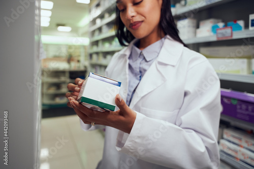 Beautiful young female working in chemist wearing labcoat checking medicine