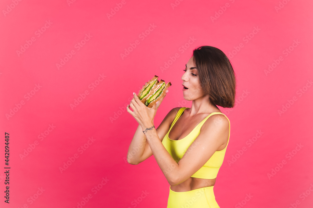 Beautiful fit woman in yellow bright fitting sportswear on pink background happy hold healthy avocado sandwich Beautiful fit woman in yellow bright fitting sportswear on pink background happy hold healthy avocado sandwich