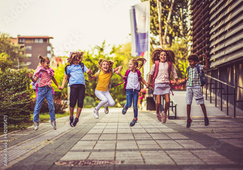 Group of elementary age schoolchildren jumping in schoolyard.