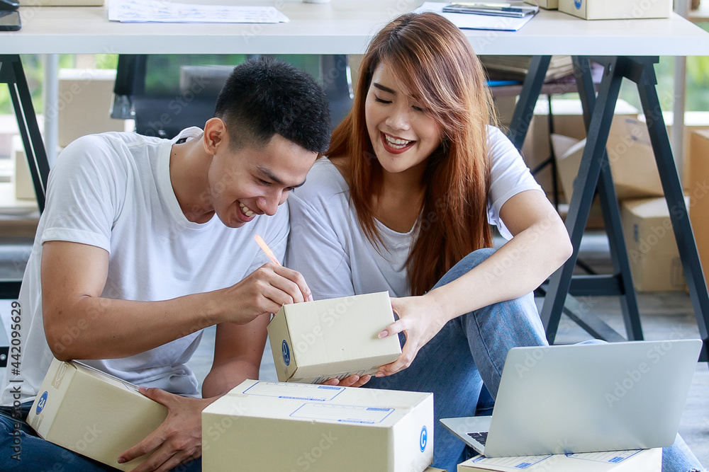 in office of delivery service business, man amused and correcting his customer address on packing box given from woman colleague that laughing at that mistake in office of delivery service business, man amused and correcting his customer address on packing box given from woman colleague that laughing at that mistake