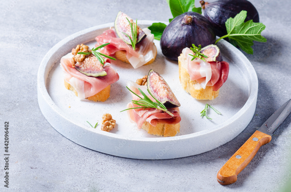 Bruschetta with raw ham, fig and rosmarin on light background.