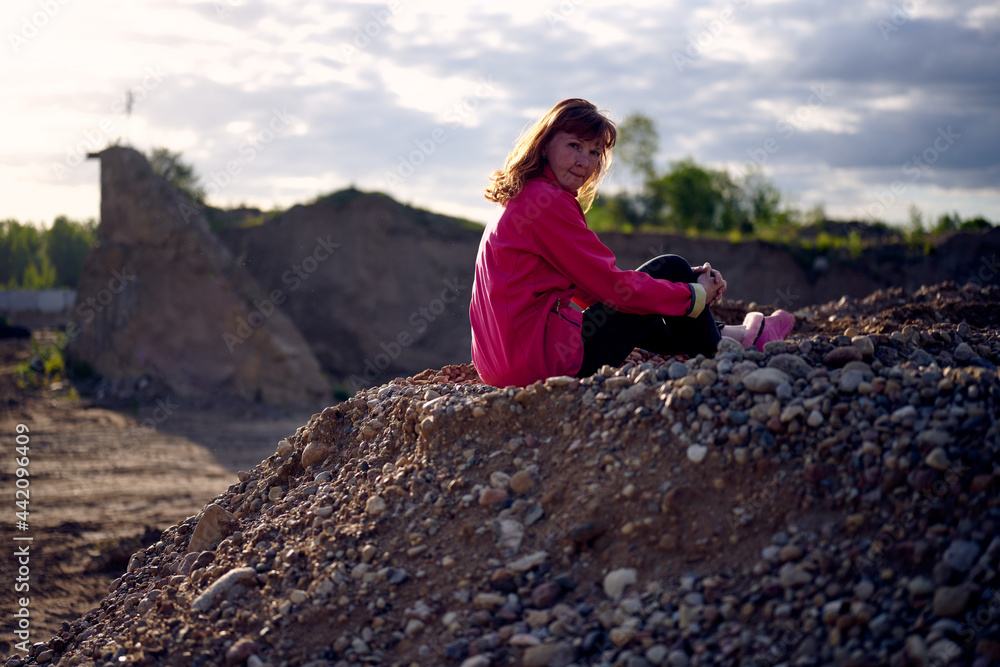Photo of a caucasian woman outdoors sitting on a sandy mountain against the background of a sunset sky in backlight