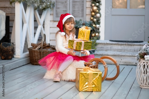 Portrait of a pretty little Santa girl with golden gift-boxes. Merry Chistmass and Happy New Year. Kids Christmas. photo