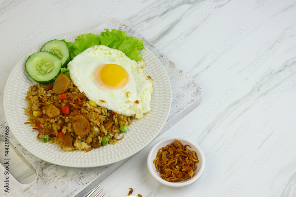 Nasi Goreng or Fried Rice, one of Indonesian popular food, topping with sunny side up egg, cucumber slices, lettuce and crackers. Top view, copy space for text.