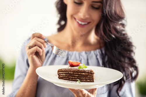 Layered brown adn white cake with strawberry and mint leaf on top held by a woman with a fork