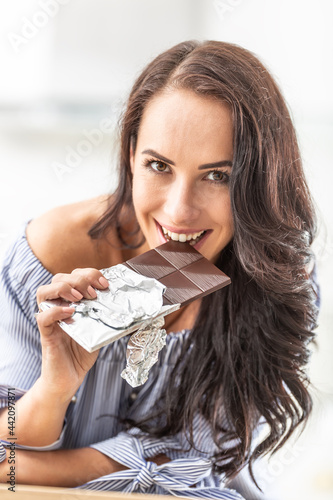 Seductvely looking woman bits off a chocolate bar  smiling
