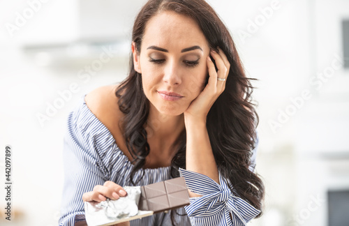 фотографія Woman thinks whether to eat or not to eat an unpacked bar of chocolate