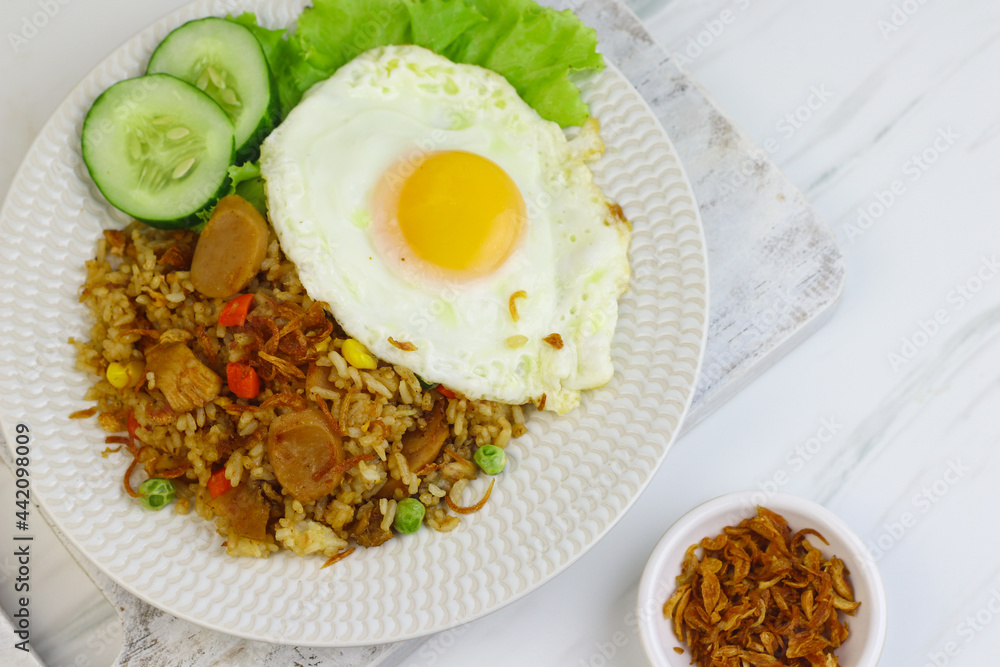 Nasi Goreng or Fried Rice, one of Indonesian popular food, topping with sunny side up egg, cucumber slices, lettuce and crackers. Top view, copy space for text. Nasi Goreng or Fried Rice, one of Indonesian popular food, topping with sunny side up egg, cucumber slices, lettuce and crackers. Top view, copy space for text.