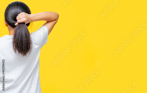 Back view of Asian woman holding damaged hair on yellow background with copy space. Split ends hair problem in woman. Dry and brittle black long hair needs shampoo and conditioner for spa treatment. photo