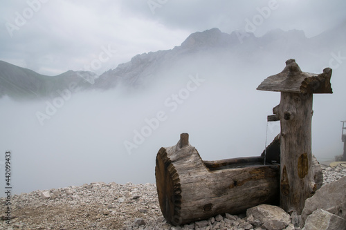 dichter Nebel in den Bergen mit Holztrog im Vordergrund