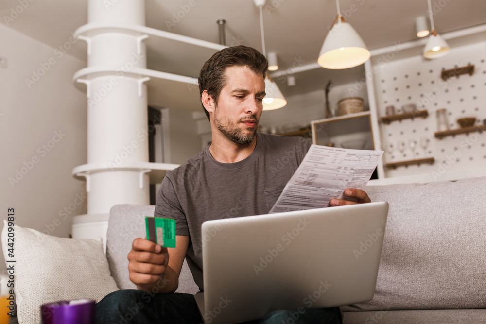 Handsome man holding credit card and using laptop at home Handsome man holding credit card and using laptop at home