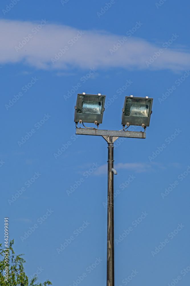The upper part of the mast of street lighting on the background of the blue sky The upper part of the mast of street lighting on the background of the blue sky