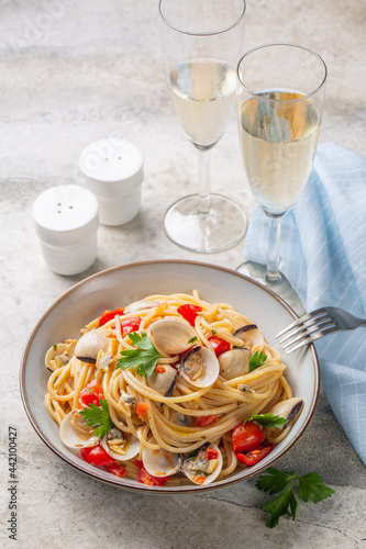 Italian dinner, seafood pasta with clams or spaghetti alle vongole and white wine glases. Light stone background, vertical image.