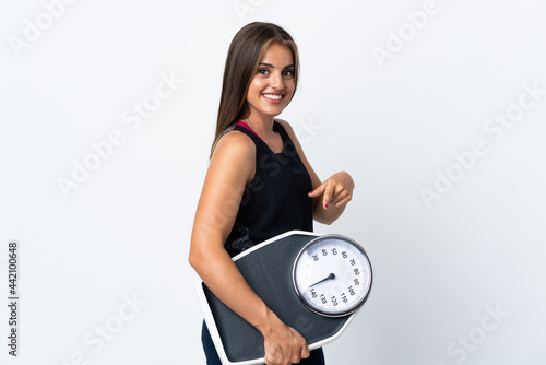 Young Uruguayan woman isolated on white background holding a weighing machine and pointing it