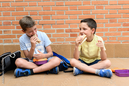 Billede på lærred Two school boys happily eating a sandwich during school recess.