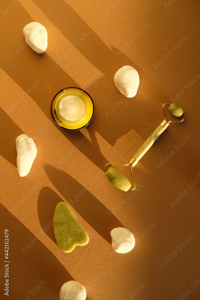 Guasha and jade stone face roller on brown background. Facial skin care concept.