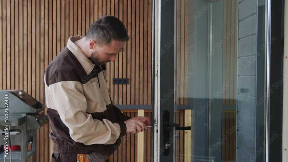 Slowmo medium shot of handyman in uniform using screwdriver and repairing door lock Slowmo medium shot of handyman in uniform using screwdriver and repairing door lock