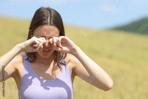Allergic woman scratching eyes in a wheat field
