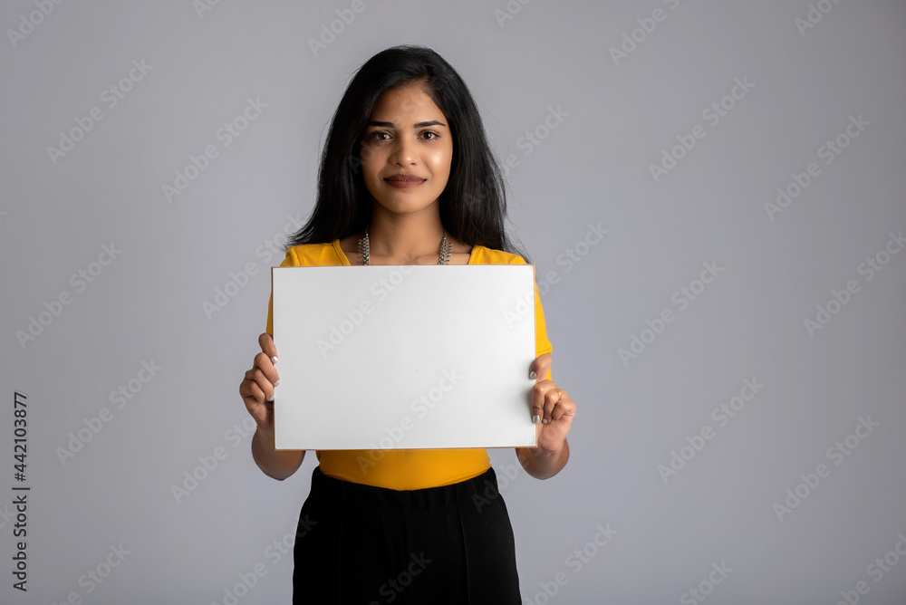 A young girl or businesswoman holding a signboard in her hands on a gray background. A young girl or businesswoman holding a signboard in her hands on a gray background.