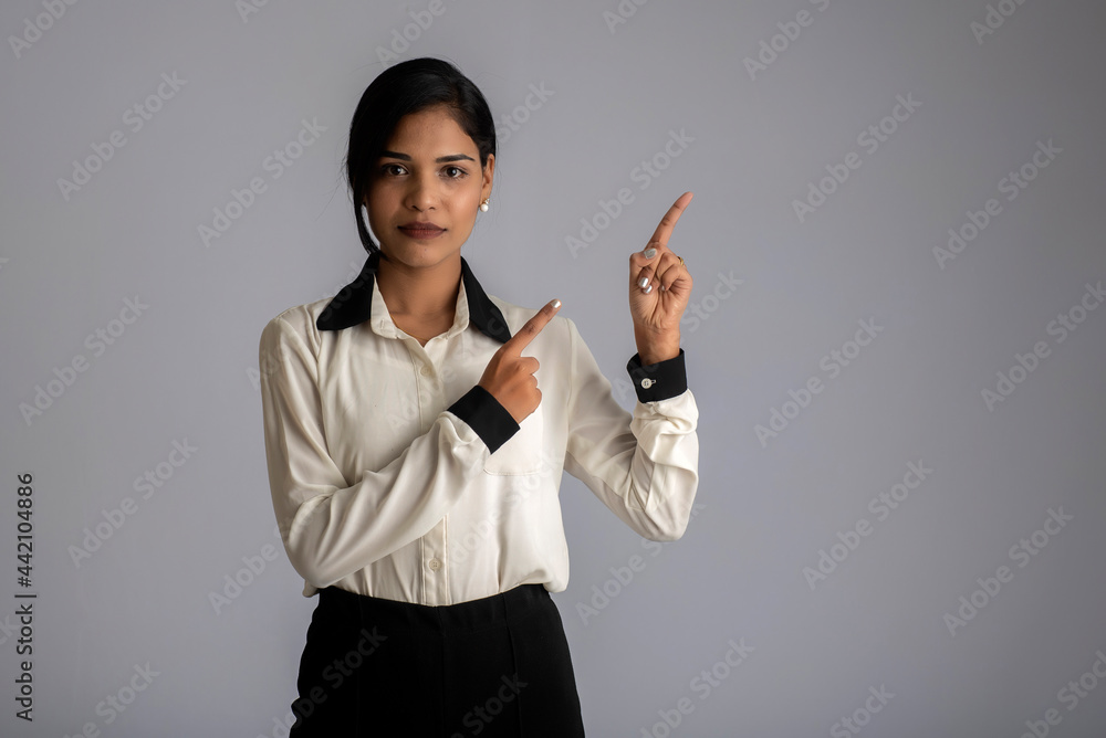 Young smiling girl pointing fingers to copy space on a grey background Young smiling girl pointing fingers to copy space on a grey background