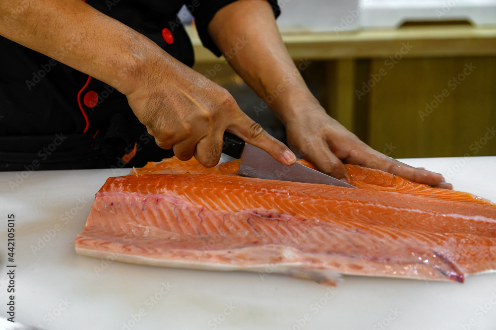 Fresh salmon fillet close-up on white cutting board table while filleting or slicing by chef in cooking room. Selection focusing on hand while slicing with Soft focusing shooting.