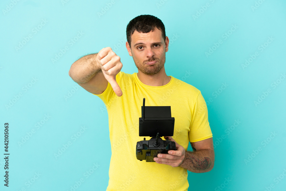Brazilian man holding a drone remote control over isolated blue background showing thumb down with negative expression Brazilian man holding a drone remote control over isolated blue background showing thumb down with negative expression
