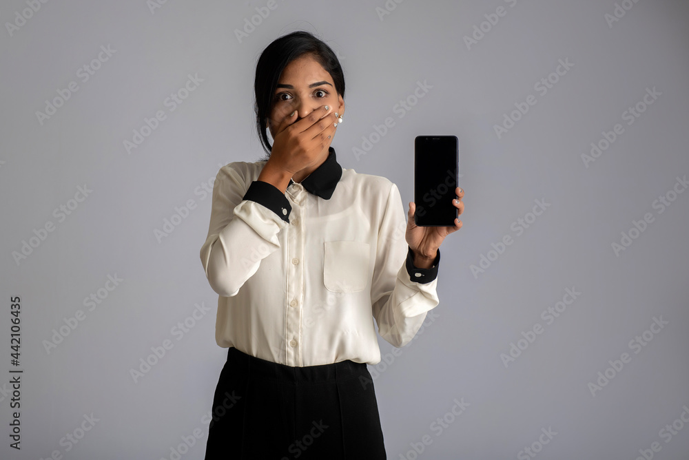 Young beautiful woman holding and showing blank screen smartphone or mobile or tablet phone on a gray background. Young beautiful woman holding and showing blank screen smartphone or mobile or tablet phone on a gray background.