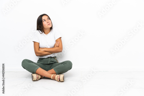 Teenager girl sitting on the floor making doubts gesture while lifting the shoulders