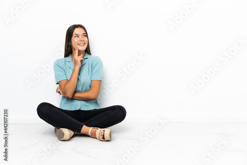 Teenager girl sitting on the floor thinking an idea while looking up
