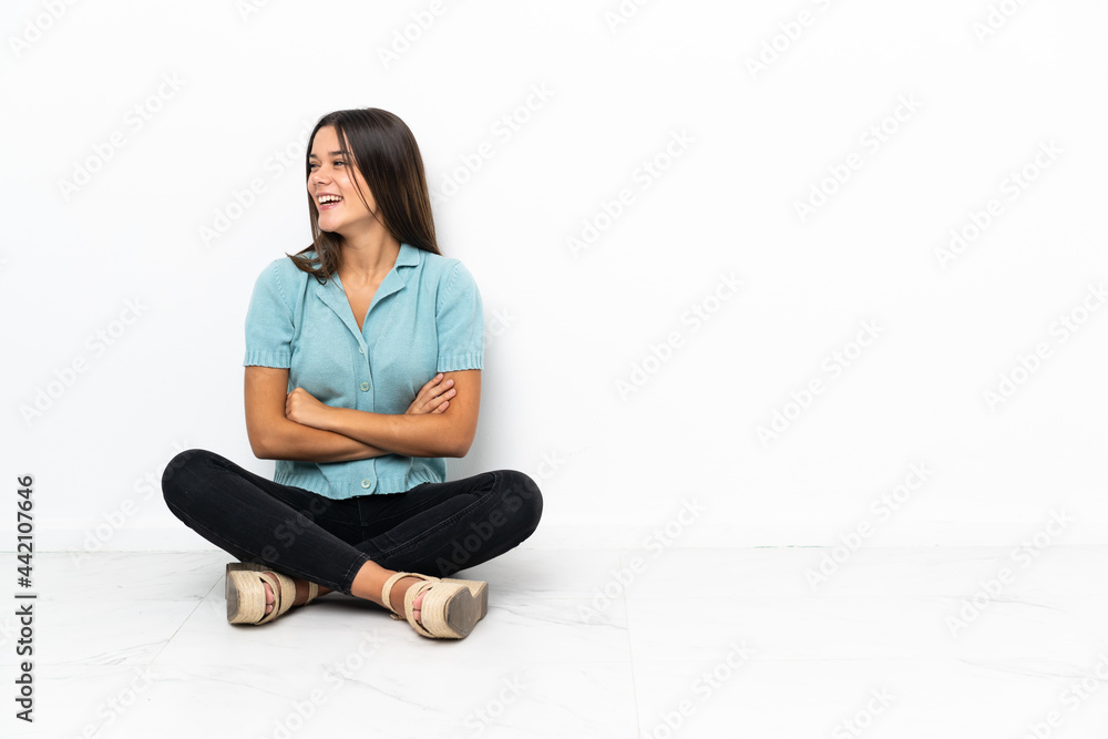 Teenager girl sitting on the floor with arms crossed and happy